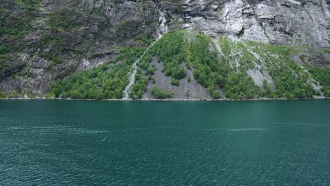 massive-Geiranger-Fjord,-as-seen-from-a-cruise-ship,-big-mountains-ranging-out-of-the-blue-water-in-4k