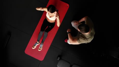 Top-down-rotating-drone-shot-of-sporty-woman-exercising-on-mat-with-personal-trainer