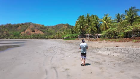 Slow-motion,-follow-Drone-Aerial-footage-of-man-on-Wild-Tropical-Island,-sandy-Beach-in-Costa-Rica-With-Palm-Trees-and-Rainforest-Landscape,-Punta-Islita