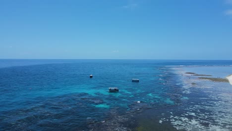 Blick-über-Ein-Barriereriff-In-Richtung-Tauchboote,-Die-Im-Blauen-Wasser-Einer-Tropischen-Insel-Festgemacht-Sind