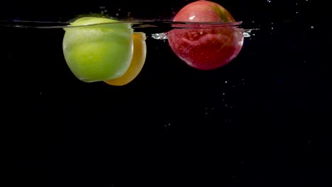 Beautiful-yellow,-green,-and-red-apples-floating-in-water-in-slow-motion