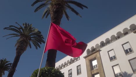 Bandera-Marroquí-Ondeando-Bajo-Palmeras-Frente-A-Edificios-Coloniales-En-Rabat-Marruecos
