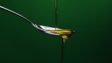 Static-shot-of-spoon-over-which-oil-is-poured-against-green-background