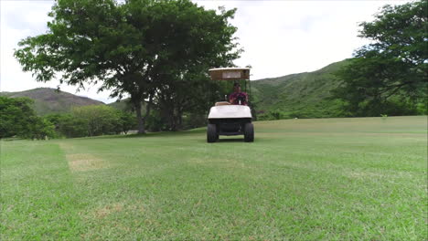 AERIAL-SLOW-MOTION:-Low-aereal-shot-of-man-driving-golf-cart-at-green-golf-course