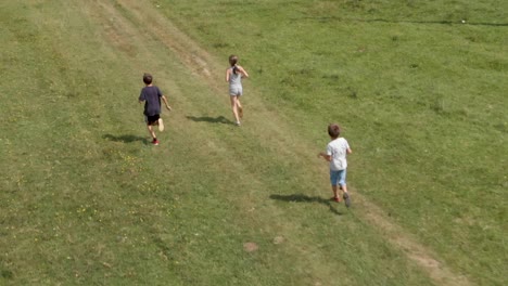 Children-run-and-play-in-green-field---aerial-slow-motion