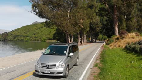 SLOWMO---Luxury-minivan-driving-on-the-coast-of-Lake-Wakatipu,-Queenstown,-New-Zealand