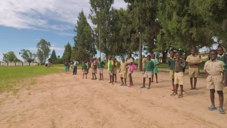 Laufen-Durch-Eine-Menge-Afrikanischer-Kinder,-Die-Ein-Fußballspiel-Außerhalb-Ihrer-Schule-Sehen,-Zeitlupe