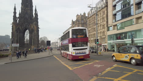 Pan-down-from-the-Scott-Monument-to-Princes-street-looking-west-with-public-buses-and-taxis-passing-by-on-a-sunny-day,-Edinburgh,-Scotland