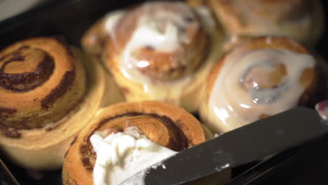 Close-up-knife-spreading-sweet-icing-on-warm-homemade-cinnamon-buns