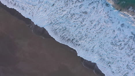 Diagonal-drone-footage-of-dynamic-ocean-waves-coming-ashore-on-sand-beach
