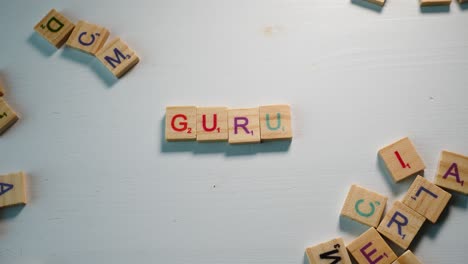 A-table-with-scattered-wooden-letters-and-a-person-spelling-Guru