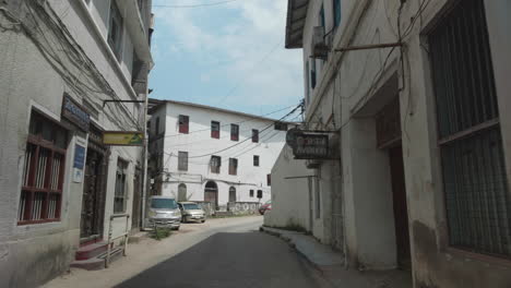 Old-narrow-street-of-Zanzibar-Stone-Town-with-bars-and-restaurants-signs-on-the-walls-and-cars-passing-by
