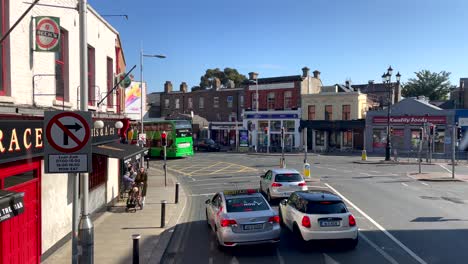 POV-Ansicht-Vom-Busfenster-Aus,-Die-Den-Verkehr-Auf-Der-Straße-Im-Zentrum-Von-Dublin-An-Sonnigen-Tagen-Zeigt---Taxi-Und-Autos,-Die-Auf-Der-Straße-Zwischen-Pub-Clubs-Und-Markt-Fahren