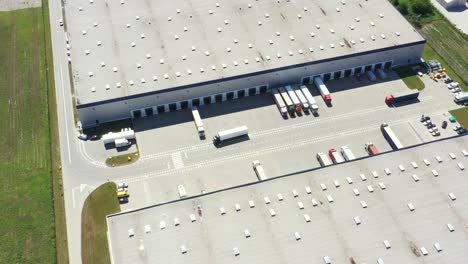 Aerial-Shot-of-Industrial-Warehouse-Loading-Dock-where-Many-Truck-with-Semi-Trailers-Load-Merchandise