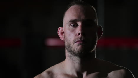 Dark-lit-medium-close-up-of-a-young-male-mixed-martial-artist-intensely-looking-at-the-camera-after-a-training-session