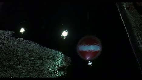 Reflection-in-pothole-filled-with-water-of-no-entry-sign-on-a-road-at-night-in-Sheffield,-South-Yorkshire