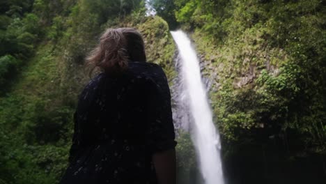 Low-angle-shot-of-a-women-standing-in-front-of-a-huge-waterfall-and-beeing-impressed-by-the-nature-creation