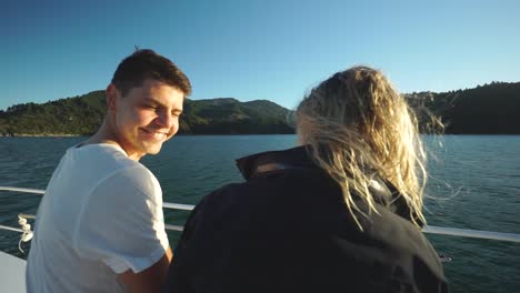 Young-couple-sitting,-talking-and-enjoying-evening-during-sunset-on-boat-in-Marlborough-Sounds,-New-Zealand