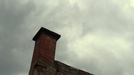 Smoke-coming-out-from-a-brick-chimney,-clouds-moving-fast-in-the-background