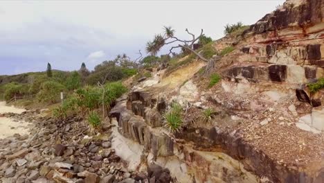 Aerial-drone-rising-shot-up-a-rocky-cliff-with-spiky-trees-to-reveal-Mt-Coolum