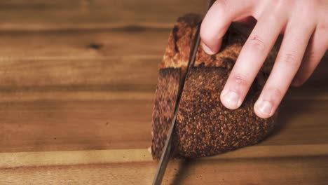 Static-close-up-shot-of-a-tasty,-crusty,-delicious-and-freshly-baked-Sourdough-loaf-being-slice-by-a-caucasian-male-on-a-wooden-chopping-board