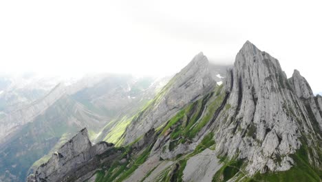 Aerial-flyover-over-the-cliffs-of-Schafler-ridge-in-Appenzell,-Switzerland-away-from-Altenturm-peak-on-a-cloudy-summer-day-with-a-view-of-one-of-Switzerland's-most-popular,-yet-dangerous-hiking-trails