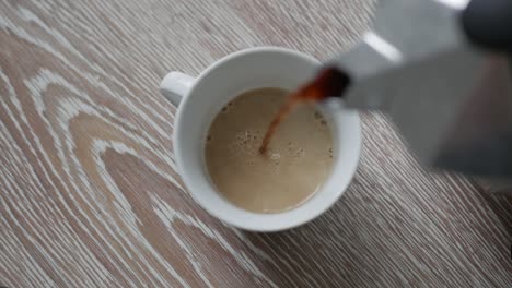 Pouring-hot-coffee-from-Bialetti-Moka-Express-into-small-cup-with-milk