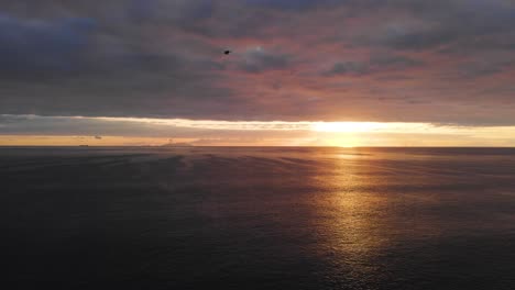 Bird-flying-over-a-calm-ocean,-against-a-cloudy-sunrise