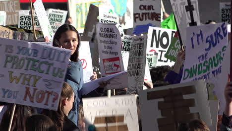 UK-February---A-female-student-sits-on-shoulders-using-a-phone-while-surrounded-by-placards-on-a-climate-change-protest