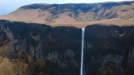 Aerial-backwards-view-of-waterfall-in-an-Icelandic-mountain-landscape
