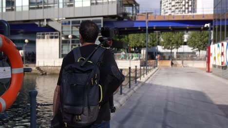 Young-man-carrying-camera-and-tripod-on-his-way-to-shoot-video-in-the-city