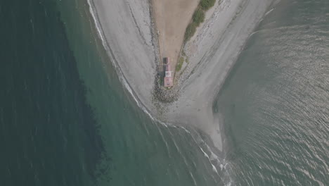 Aerial-footage-of-a-beach-head-with-a-lighthouse-at-the-tip-of-the-landmass-slowly-ascending-in-Seattle,-WA
