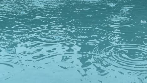 Rain-drops-splashing-into-clean-pool-of-aquamarine-water,-close-up-slow-motion