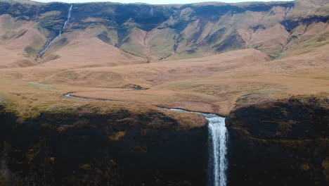 Aerial-backwards-view-of-a-sheer-mountain-with-a-waterfall