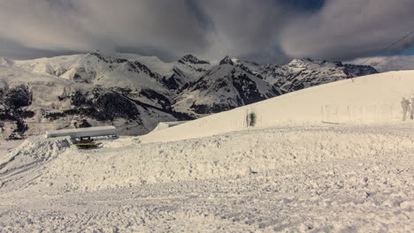 Time-lapse-of-white-clouds-flying-over-snowcapped-mountain-peaks---snow-groomers-prepare-snow-park-for-Suzuki-Nine-Knights-event,-Livigno,-Italy