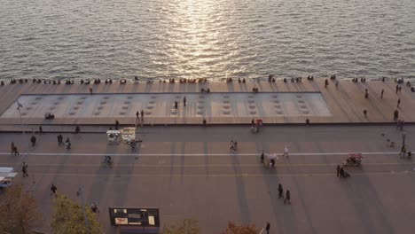 Aerial---People-passing-by-in-Thessaloniki-seaside-walkway-at-sunset