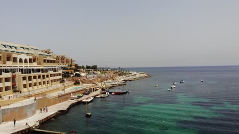 Holiday-boats-swaying-in-calm-waves-of-emerald-blue-Mediterranean-sea-next-to-Marina-Hotel-Corinthia-Beach-Resort-in-Saint-George's-Bay,-St-Julian's,-Malta