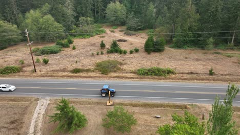 Static-drone-shot-of-a-tractor-mowing-the-weeds-in-the-ditches-of-a-small-town-in-America