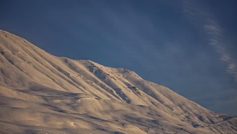 Timelapse-shot-of-sunrise-light-reflected-on-snowy-mountain-slope---cloud-movement-in-white-snow-landscape-with-blue-sky