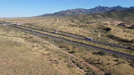 Aerial-view,-Semis-and-Cars-driving-on-Highway-in-desert,-Mountains-in-Background