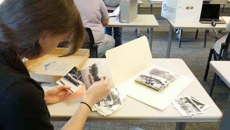 A-female-college-student-researcher-sorts-through-historical-photos-of-antiques-and-memories-on-her-desk-as-part-of-an-archival-research-project-for-an-art-class