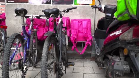 Bicicletas-Y-Bolsas-De-Entrega-De-Alimentos-Alineadas-Contra-La-Pared-En-Un-Entorno-Urbano