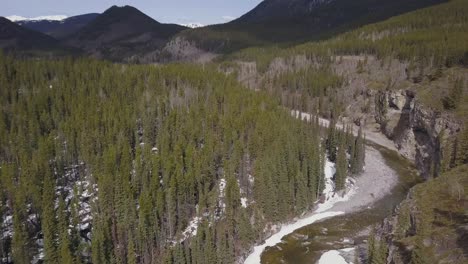 Spring-flyover-of-boreal-river-canyon-with-mountains-in-the-background