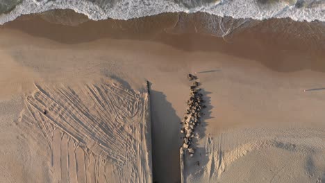 People-causing-long-shadows-passing-waves-coming-in-on-a-pristine-Leblon-beach-with-the-mouth-of-a-drainage-canal-contrived-of-partly-constructed-and-partly-placed-rocks-leading-to-the-city-lake