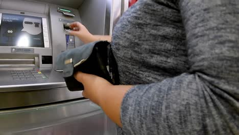 Woman-operating-a-ATM-automated-teller-machine,-end-of-operation,-she-takes-out-her-card-and-receipt-and-packs-it-away-in-her-purse