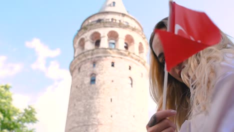 Zeitlupe:-Attraktives-Junges-Schönes-Mädchen-Macht-Selfie-Und-Winkt-Türkische-Flagge-Vor-Galata-turm,-Einem-Beliebten-Wahrzeichen-In-Istanbul,-Türkei