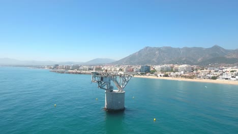 Aerial-view-of-cable-beach-marbella,-big-abandoned-object-in-the-sea,-tower-in-sea