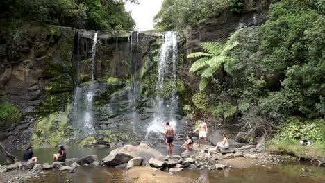 SLOWMO---Group-of-young-people-standing-by-Mokoroa-Falls,-Auckland,-New-Zealand