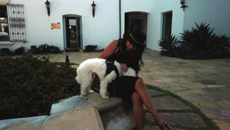 Walking-towards-female-petting-white-small-dog-in-front-of-a-fountain-with-flowers-at-wine-tasting-room,-Los-Angeles