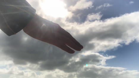 Close-up-shot-of-a-man-hand-with-sun-rays-piercing-through-a-cloudy-blue-sky-as-background